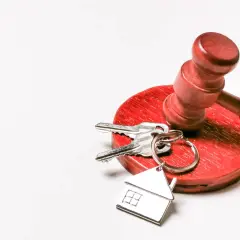 Młotek sędziowski i klucze z breloczkiem w kształcie domu. Symbolizuje to sytuację, gdy najemca nie płaci czynszu i sprawa trafia do sądu.