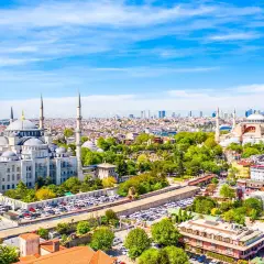 Widok na Stambuł, miasto łączące Europę i Azję, z Błękitnym Meczetem i Hagia Sophia. W tle nowoczesne wieżowce, a na pierwszym planie zielone drzewa i zabudowa miejska.
