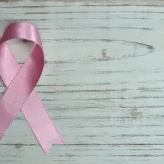 Różowa wstążka na białym, drewnianym tle. Symbol nadziei i wsparcia, przypominający o mądrych słowach otuchy w chorobie.