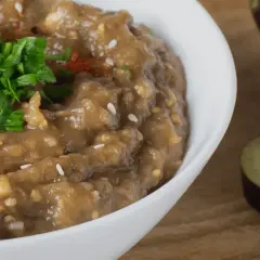 En krämig baba ganoush toppad med färsk persilja och paprikapulver. Bredvid syns skivade auberginer.