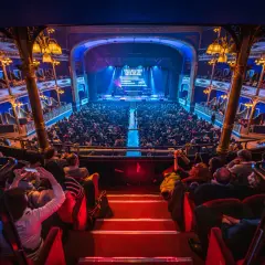 Un pubblico numeroso assiste a uno spettacolo nel Teatro Colosseo di Torino, con luci soffuse e un palco illuminato.