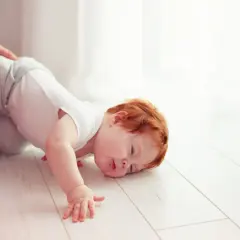 Un bimbo con capelli rossi è caduto dal letto. Un adulto lo tiene per la gamba. Non c'è motivo di preoccuparsi, è solo un piccolo capitombolo.
