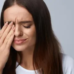 Kobieta zamyka oczy, pocierając je dłonią. Może to być jeden z objawów zespołu Sjogrena, który powoduje suchość oczu.