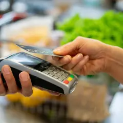 Une main approche une carte bancaire d'un terminal de paiement pour un paiement sans contact.