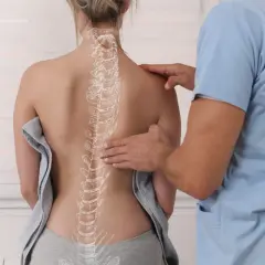 Fizjoterapeuta bada kręgosłup pacjentki, na którym widoczny jest zarys kifozy piersiowej.