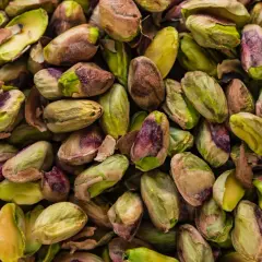 Un primo piano di pistacchi sgusciati, con sfumature verdi e violacee, pronti per essere gustati. Questi frutti secchi provengono da un **maggior produttore di pistacchi**.