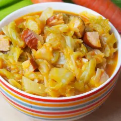 Pyszny bigos z młodej kapusty z kiełbasą, podany w kolorowej miseczce. Obok widać marchewkę i selera.