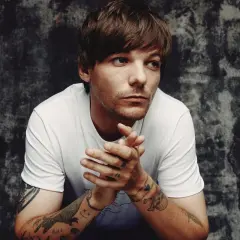 Louis Tomlinson zamyślony, z dłońmi złożonymi przed sobą. Fani czekają na jego nadchodzące wydarzenia.
