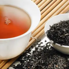 Eine Tasse dampfender Tee ohne Teein neben einer Schale voller trockener Teeblätter.