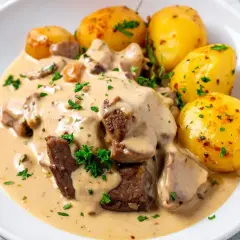 Mięso w kremowym sosie seczuańskim z pieczonymi ziemniaczkami, posypane natką pietruszki.