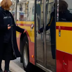 Kobieta z telefonem w ręku zbliża się do autobusu, by skasować bilet elektroniczny.