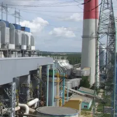 Duże budynki elektrowni z niebieskimi elementami, wysokie kominy z czerwonymi pasami i linie energetyczne.