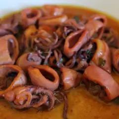 Calamares en salsa, tiernos y jugosos, con sus tentáculos enrollados, nadan en un rico caldo dorado.