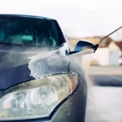 Pokazano, jak myć auto na myjni bezdotykowej. Woda pod ciśnieniem spływa po masce i reflektorze ciemnego samochodu.