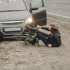 Kobieta w kasku leży obok przewróconego roweru, obok stoi samochód z otwartymi drzwiami. Wygląda na to, że doszło do ucieczki z miejsca kolizji.