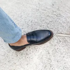 Un homme en jean bleu porte une chaussure de ville marine. L'outil à côté suggère une envie de ressemeler chaussures.