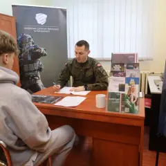 Młody mężczyzna siedzi przed żołnierzem, który wypełnia dokumenty. To rozmowa kwalifikacyjna w Wojskowym Centrum Rekrutacji.