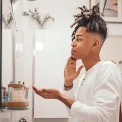 Mann mit Dreadlocks im Spiegel, der sich die Haut richtig reinigen möchte.