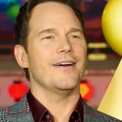 Chris Pratt, gwiazda wielu filmów, uśmiecha się na tle czerwonych lampionów i żółtej dekoracji.