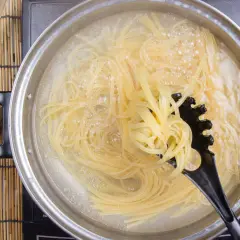 Spaghetti kochen in sprudelndem Wasser. Ein schwarzer Pastalöffel hebt eine Portion heraus, um zu zeigen, wie kleben spaghetti nach dem kochen nicht zusammen.