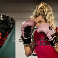 Mikaela boxare i rosa handskar, redo för träning. Hennes blick är fokuserad, med dreadlocks som ramar in ansiktet.