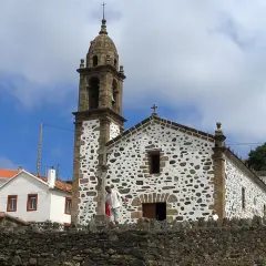 Iglesia de San Andrés de Teixido, con su campanario y fachada de piedra y cal, bajo un cielo nublado.