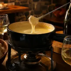 Un réchaud chauffe une fondue savoyarde crémeuse, accompagnée de pain et d'un verre de vin pour fondue savoyarde.