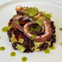 Delizioso polpo alla griglia servito su riso venere con avocado e pomodorini, condito con salsa verde.