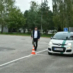 Młody mężczyzna ustawia pachołek na placu manewrowym. Biały Fiat Panda z zielonym pasem i literą "L" na dachu czeka na swój egzamin praktyczny kat B.