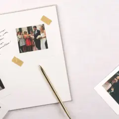Vœux de mariage manuscrits sur un album, avec des photos instantanées de la cérémonie et du couple. Un stylo doré repose à côté.