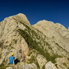 Un excursionista con casco amarillo contempla imponentes montañas, un paisaje ideal para rutas por Berga.