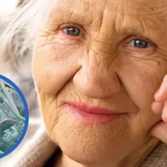 Starsza pani z zamyśloną miną, obok stos banknotów 100 zł. Czy wada wzroku a zasiłek pielęgnacyjny to temat dla niej?