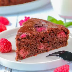 Tranche de gâteau au chocolat et framboise sans gluten, décorée de fruits frais et d'une touche de menthe.