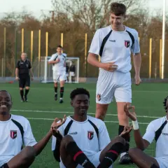 Fußballjugend in weißen Trikots sitzt im Schneidersitz auf dem Rasen, einige mit geschlossenen Augen und meditierenden Händen.