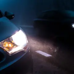 Mocna lampa led świeci jasno, rozświetlając mglistą noc i drogę. Inny samochód jedzie z przodu.