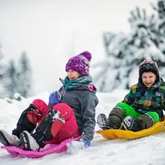 Dzieci z uśmiechem zjeżdżają na sankach po ośnieżonym stoku. Idealne miejsce, gdzie na ferie zimowe z dziećmi.