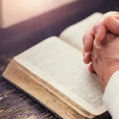 Dłonie złożone nad otwartą księgą, której strony zawierają tekst apostolski.