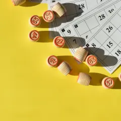 Drewniane krążki z numerami i karty do gry w bingo leżą na żółtym tle, gotowe do emocjonujących konkursów i loterii.