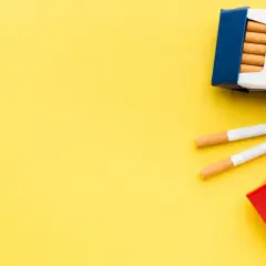 Dwie paczki papierosów, jedna niebieska, druga czerwona, leżą na żółtym tle. Dwa papierosy leżą obok. Ile papierosów do Niemiec?
