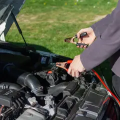 Persona conecta pinzas a la batería de un coche que no arranca.