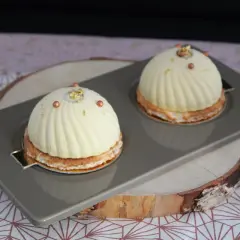 Deux dômes de dessert fruités, ornés de perles cuivrées et de feuilles d'or, reposent sur un plateau gris.