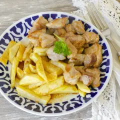 Un plato de raxo con patatas fritas, decorado con perejil fresco. Un clásico delicioso.