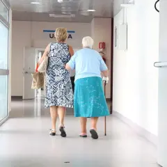 Dwie kobiety idą korytarzem szpitalnym. Jedna wspiera się laską. Być może zmierzają po świadczenia 500 plus dla chorych na raka ZUS.