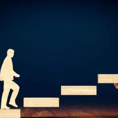 Drewniana postać wchodzi po schodkach, a dłoń podaje kolejny stopień.