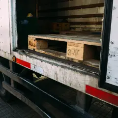 Wnętrze ciężarówki z widocznymi drewnianymi paletami, gotowymi do załadunku. Na jednej z palet widoczny napis "TCLU".