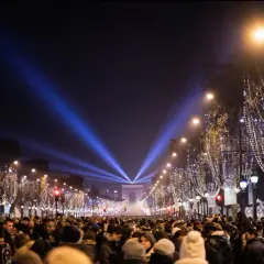 Une foule nombreuse célèbre une **soirée paris** sous les lumières bleues illuminant l'Arc de Triomphe et les arbres décorés de guirlandes.