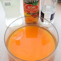 Pomarańczowy sok w dużej misie, obok karton soku multivitamin i butelka wody. Idealne składniki na orzeźwiający **jungle juice**.