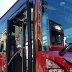 Autobus rosso con porte aperte, riflessi di palazzi sui vetri. Forse l'ultima metro della giornata, ma è un bus.