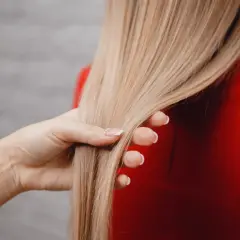 Dłoń dotyka gładkich, blond włosów. To efekt zastosowania tonera do włosów, który odświeża kolor i nadaje blask.