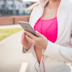 Kobieta w sportowym stroju trzyma iPhone'a, słuchając muzyki. Chcesz wiedzieć, jak włączyć Siri?